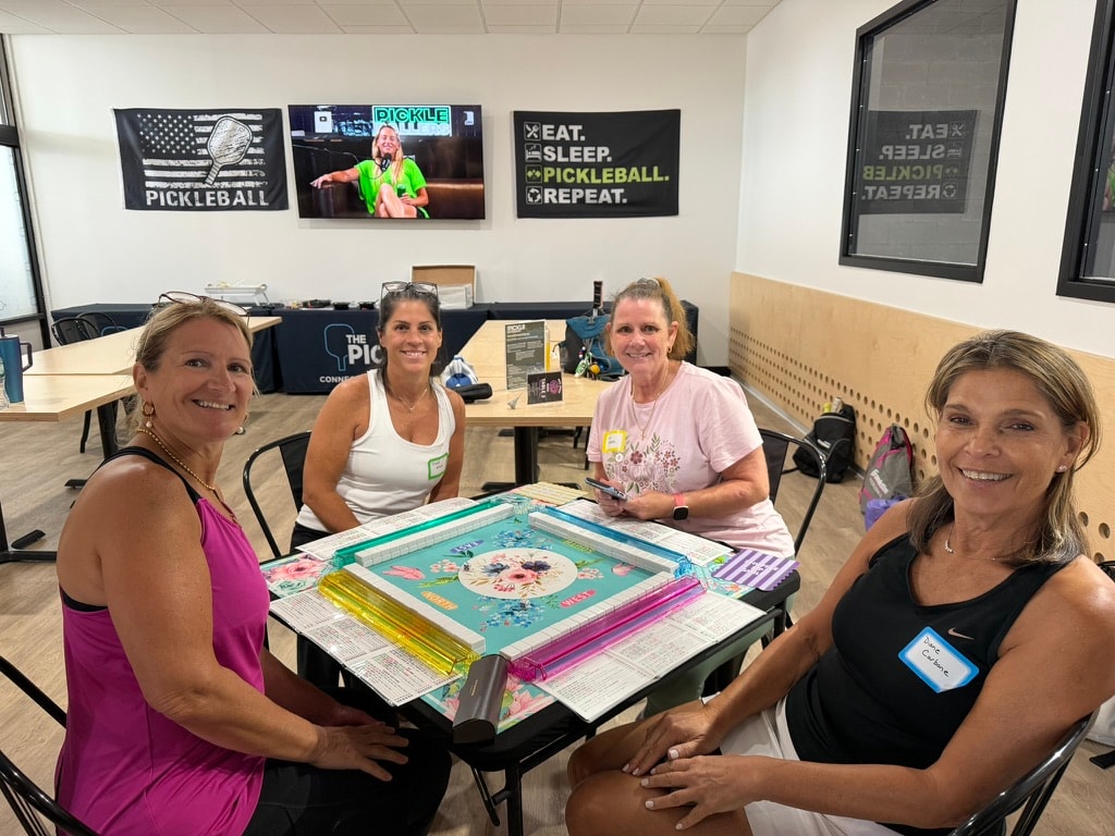 Four women playing mah jongg at a table inside The Picklr facility